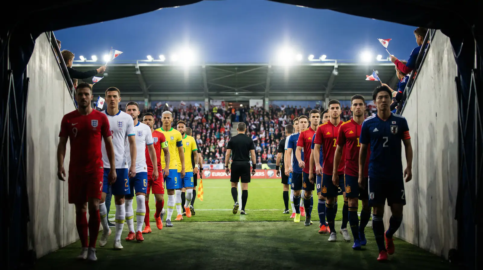 Fodboldspillere fra forskellige lande marcherer ind på banen til en VM-kamp under klart lys